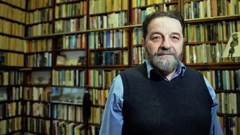 Polish journalist Konstanty Gebert poses in front of a book shelf in his home in