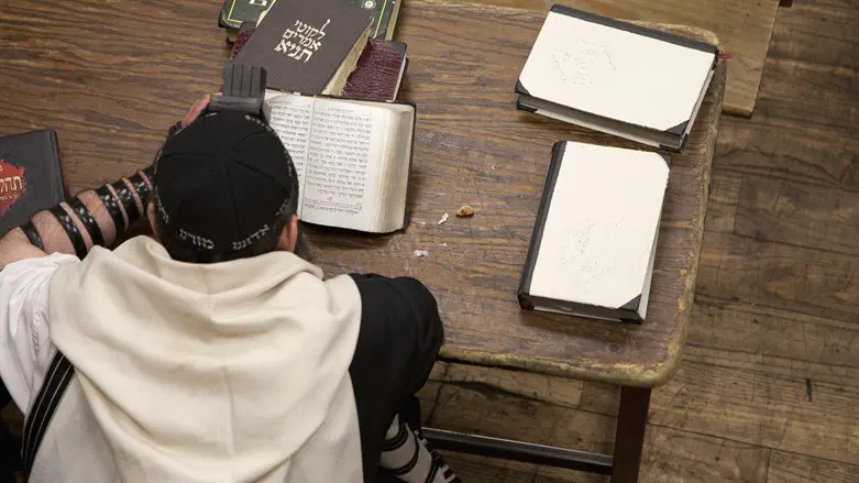 Jewish man with tefillin reading religious prayer book. 