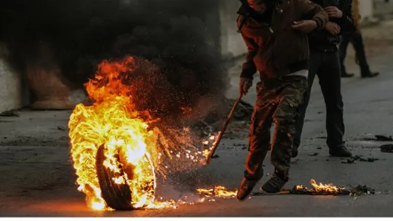 Arab rioter rolls burning tire with a stick
