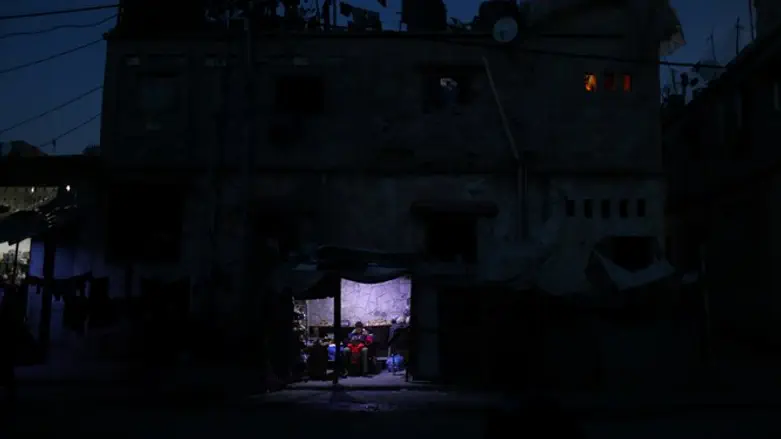 Arab sells vegetables in makeshift shop lit with lamp powered by battery during power cut 