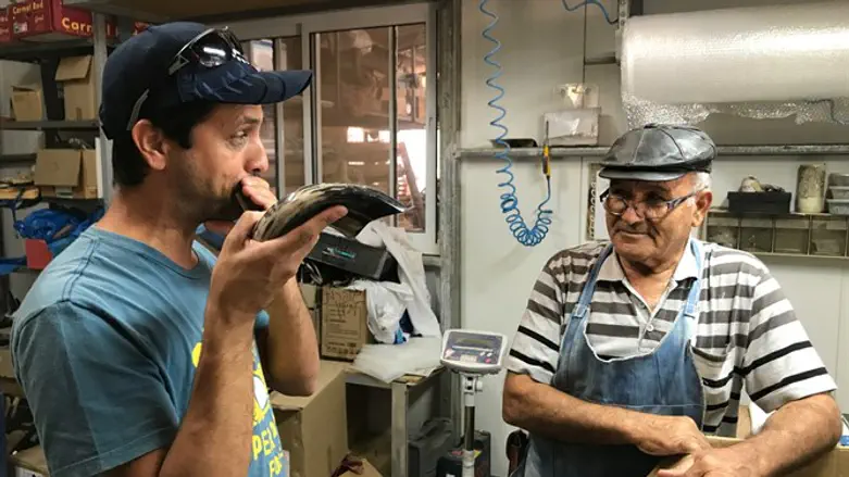 Dror Yoggev blowing a shofar while Shimon Keinan watches at his Kol Shofar factory in Giva