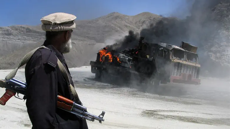 Pakistani security official stands near a burning vehicle after it was attacked